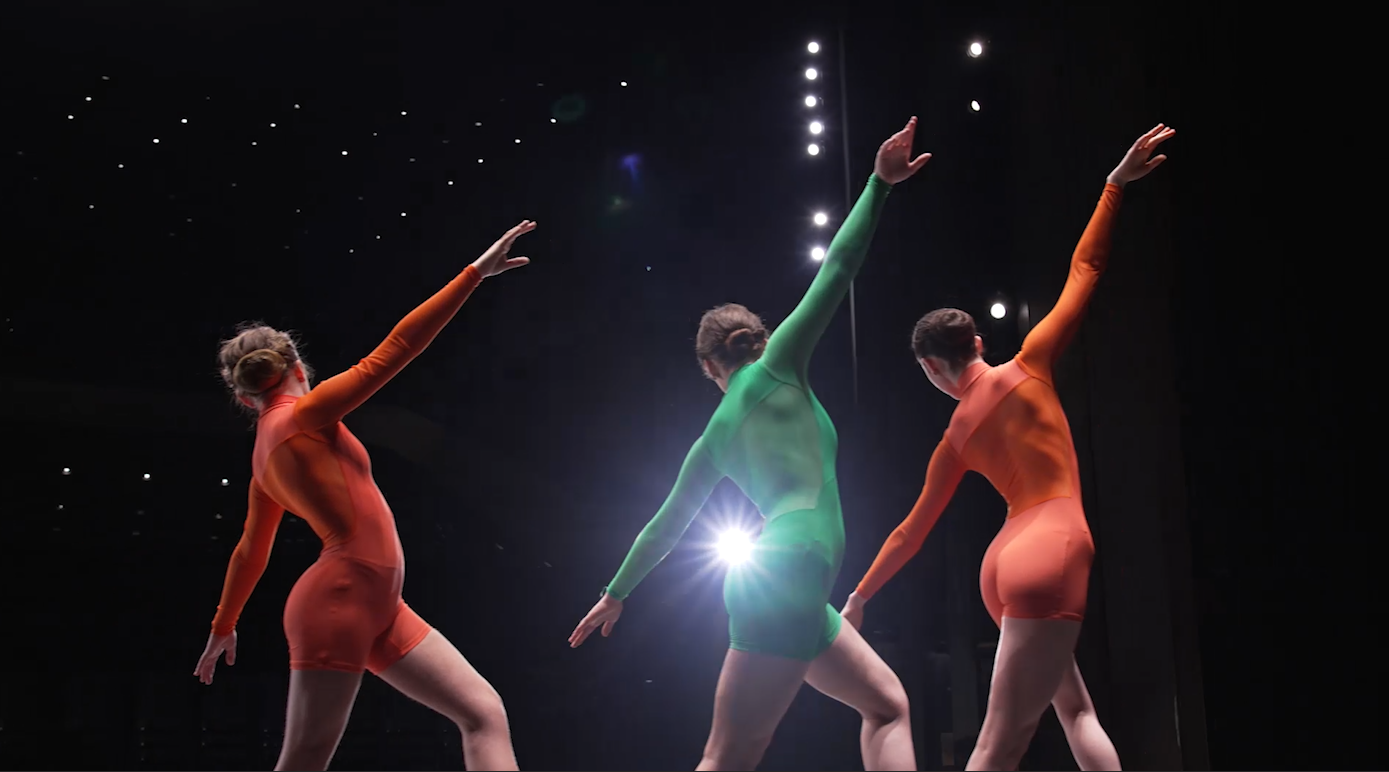 Three dancers in jewel tones dance cross the stage.